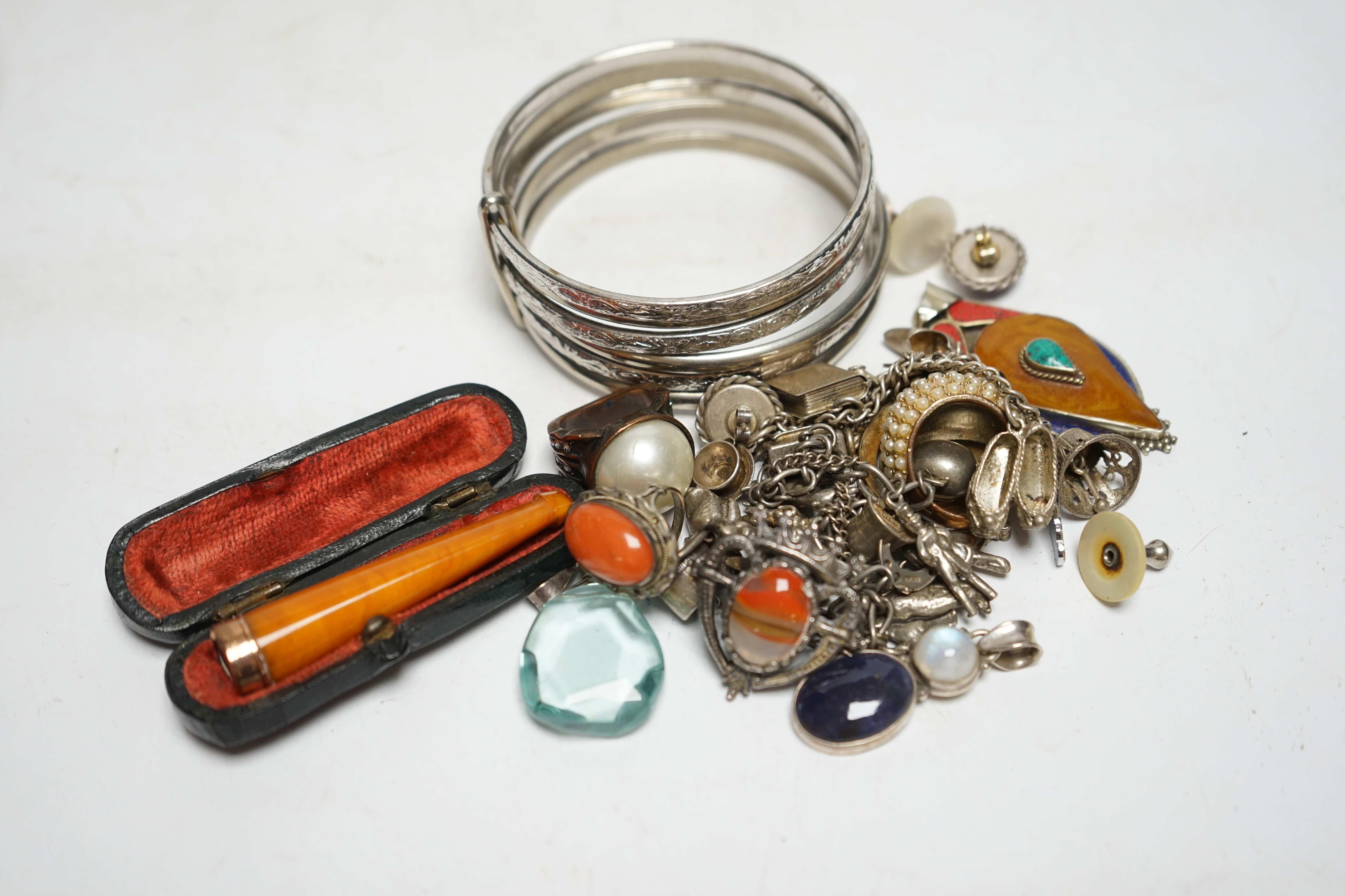 A small group of assorted white metal and costume jewellery including two charm bracelets and a cased 9ct gold mounted amber cigarette holder. Condition - poor to fair